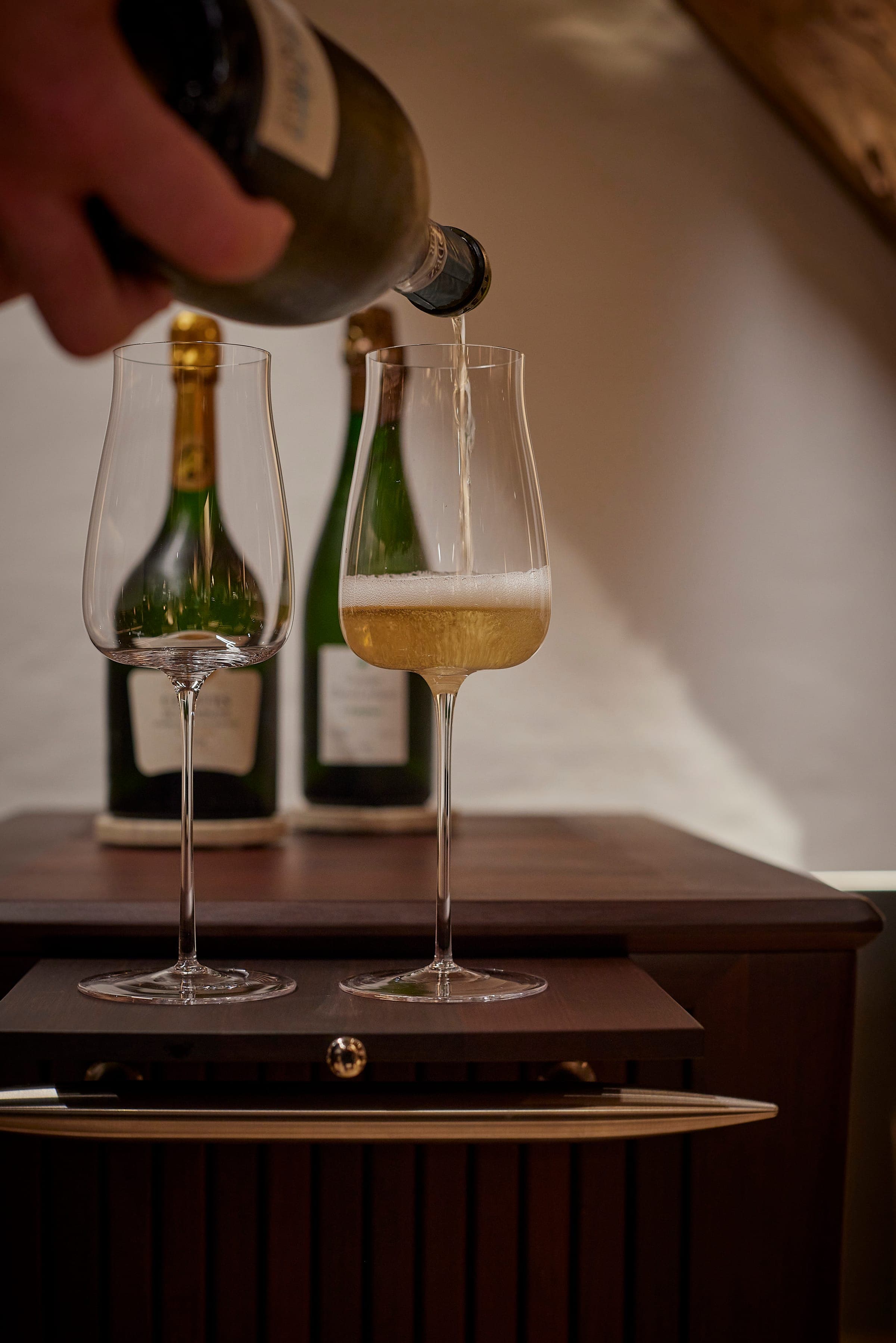 Champagne poured into a tall glass beside two bottles