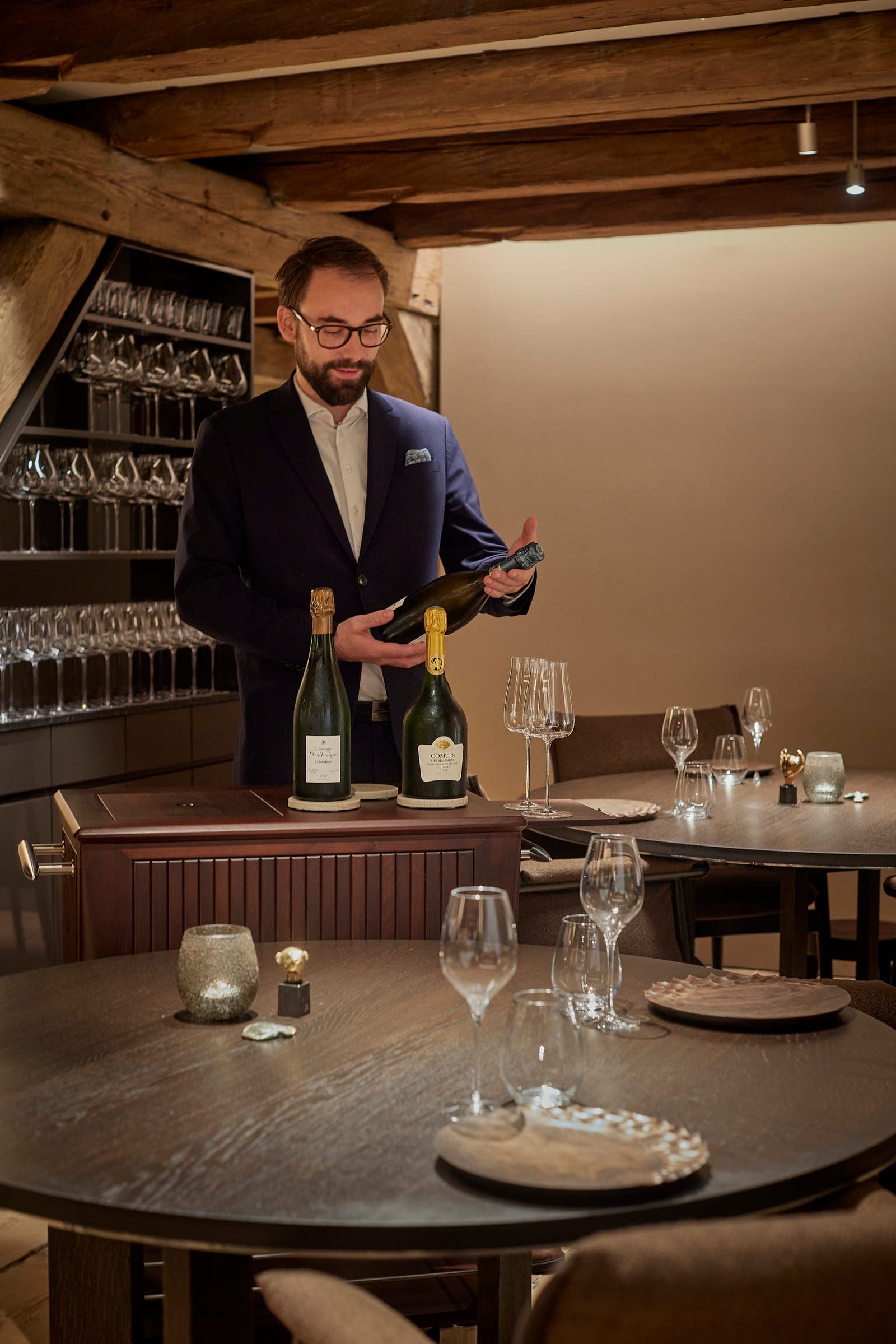 The sommelier presenting a bottle of champagne at the bar, beside a wall of glasses